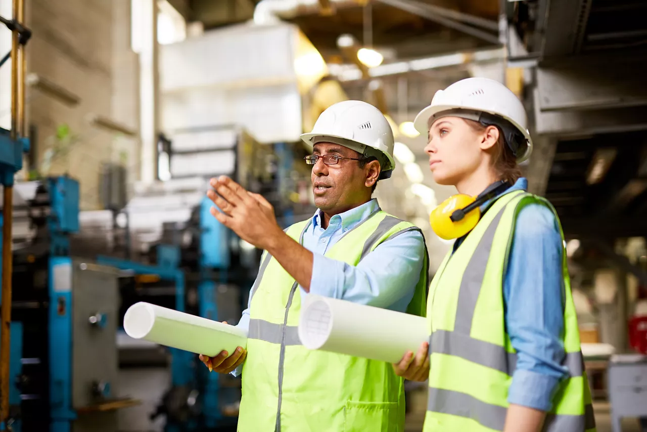 Male and female engineers in hard hats working together at a factory 