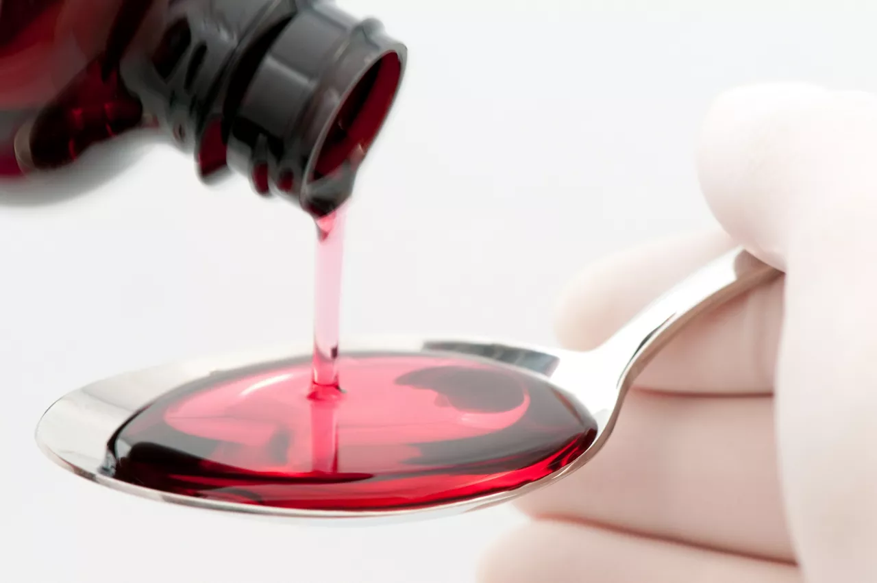 Spoonful of cough syrup being filled by person wearing latex gloves, on white background
