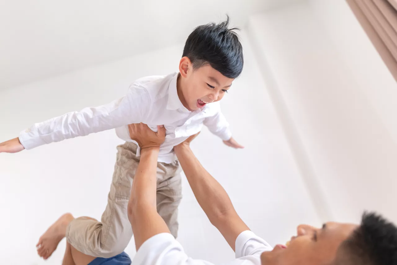 Happy father playing with son while lying on the bed at home