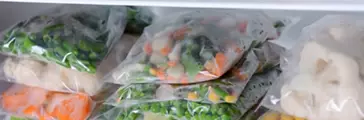 Plastic bags and containers with frozen vegetables in refrigerator