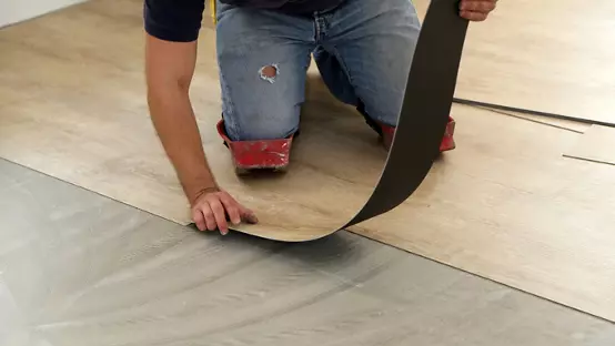 Work on laying flooring. Worker installing new vinyl tile floor.