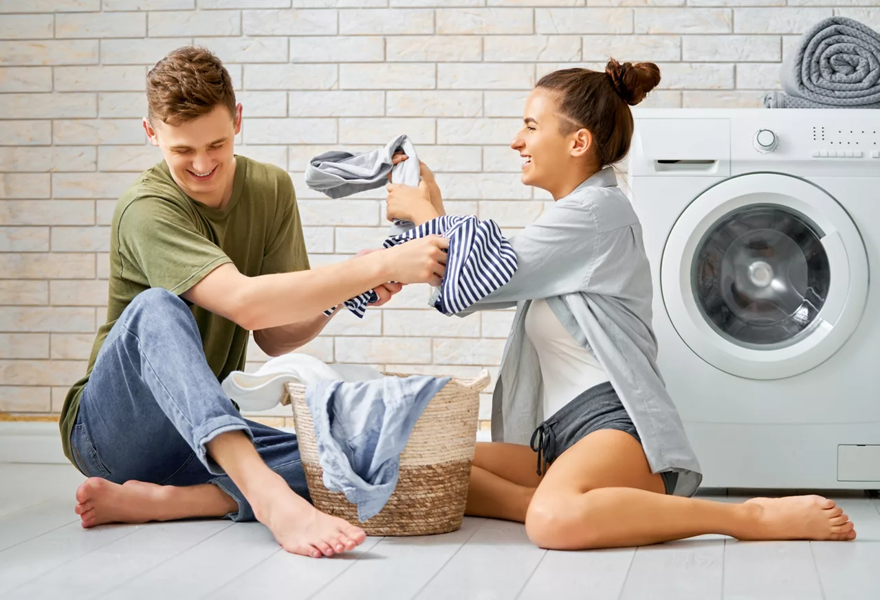 Young loving couple smiling while doing laundry at home