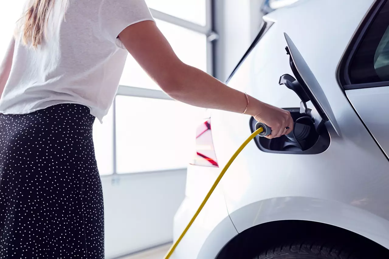 Closeup Of Woman Charging Electric Vehicle With Cable In Garage At Home