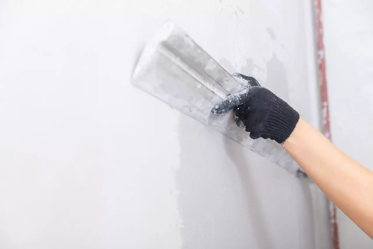 Construction worker applies plaster with trowel to concrete wall to level surface.