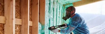 Worker spraying polyurethane foam for insulating wooden frame house.