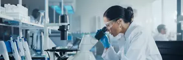 Medical Development Laboratory: Caucasian Female Scientist Looking Under Microscope, Analyzes Petri Dish Sample. Specialists Working on Medicine, Biotechnology Research in Advanced Pharma Lab