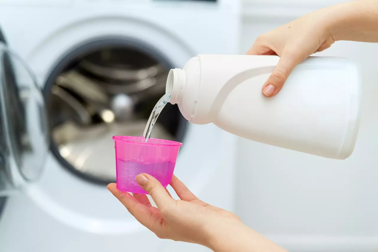 Female hand holding laundry detergent in front of open washing machine
