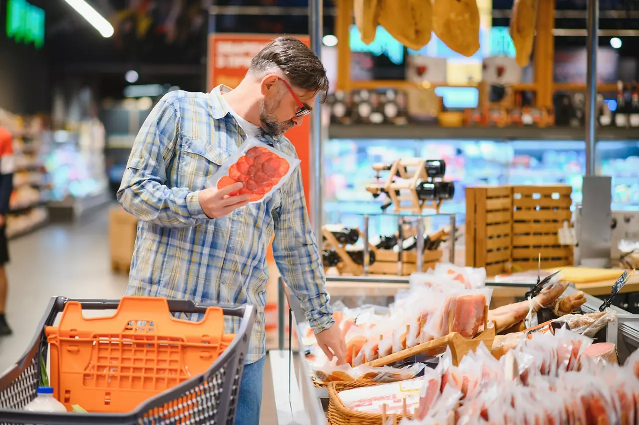 Elderly man buyer of meat department of grocery store, holding at meat sausage.