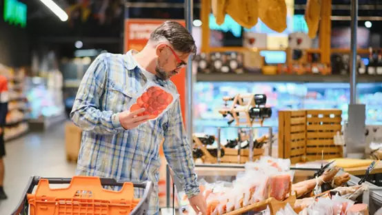 Elderly man buyer of meat department of grocery store, holding at meat sausage. 