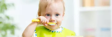 Infant toddler sitting in high chair eating with a spoon